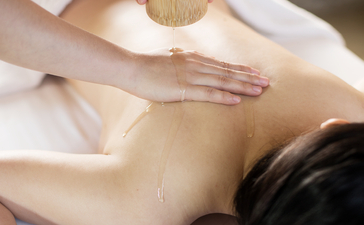 Therapist applying golden massage oil to guest's back at Amanfayun.