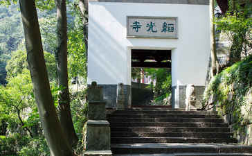 A whitewashed pavilion with traditional Chinese architecture nestled among trees at Amanfayun, featuring dark wooden steps leading to an entrance beneath overhanging branches.
