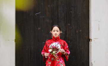 Woman in red traditional áo dài standing before dark wooden door at Amanfayun.