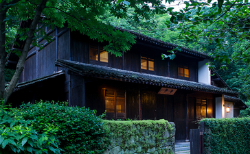 Amanfayun pavilion nestled amongst lush greenery with warm interior lighting at dusk.