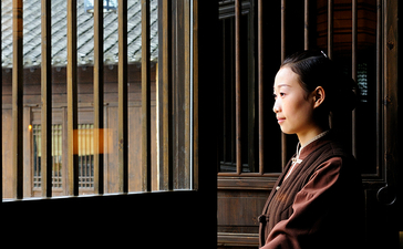 Woman standing in traditional wooden doorway at Amanfayun, filtered light creating geometric shadows.