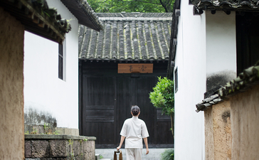 Person walking through a traditional courtyard at Amanfayun, with white-walled buildings and dark tile roofs.