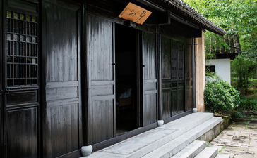 Black wooden pavilion with double doors at Amanfayun, framed by lush greenery.