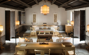 Gallery space at Amanfayun with wooden furniture and neutral tones, featuring a central table arrangement and pendant lighting.