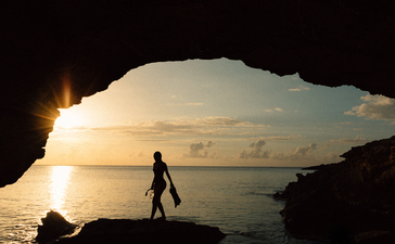 Silhouetted figure walking through a rocky cave opening at sunrise, Amanyara resort.