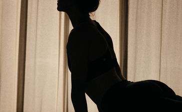 Silhouette of a woman in yoga pose at Amanyara resort, filtered sunlight through curtains behind her.