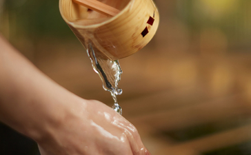 Water pours from a wooden dipper into an open hand at Amanemu resort.