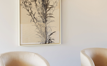 Cream curved chair with wooden side table holding spa bottles, botanical artwork above, Amanemu resort.