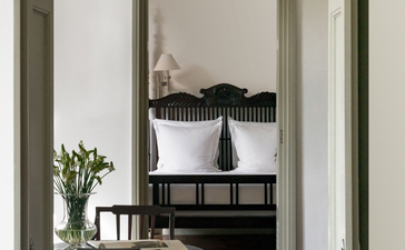 View through doorway to Amangalla bedroom with framed mirror and fresh flowers on side table.