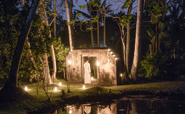Amangalla pavilion illuminated at dusk, reflected in still water amongst towering palms.