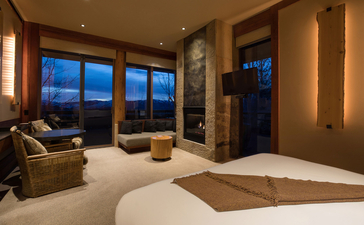 Deluxe Suite at Amangani with floor-to-ceiling windows overlooking evening mountain views, warm lighting, and contemporary furnishings.