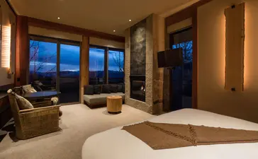 Deluxe Suite at Amangani with floor-to-ceiling windows overlooking evening mountain views, warm lighting, and contemporary furnishings.