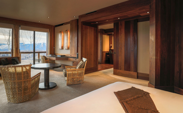 Gros Ventre Suite at Amangani with floor-to-ceiling windows overlooking mountain landscape, warm wood furnishings, and neutral tones throughout.