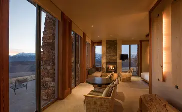 Sena Suite at Amangani with floor-to-ceiling windows overlooking mountain landscape at dusk.