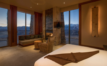 Sena Suite principal bedroom at Amangani with floor-to-ceiling windows overlooking mountain landscape at dusk.