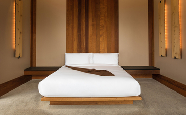 Sena Suite principal bedroom at Amangani, featuring a low wooden bed with white bedding and dark pillows.