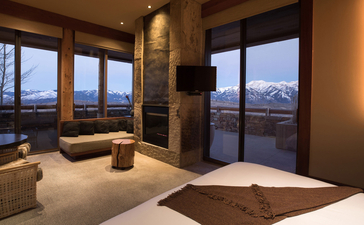Shoshone Suite bedroom at Amangani with views over mountains at dusk through floor-to-ceiling windows.