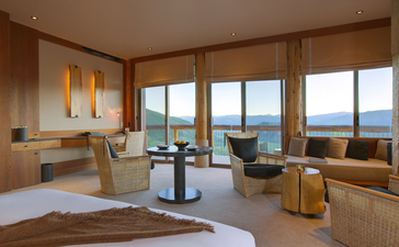 Principal bedroom at Amangani with expansive windows framing mountain views, warm wood finishes, and contemporary furnishings.