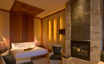 Amangani Superior Suite with fireplace and warm ambient lighting, featuring a bed and seating area.