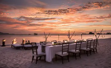 Table de salle à manger dressée sur la plage au coucher de soleil à Amanpulo, la station balnéaire.