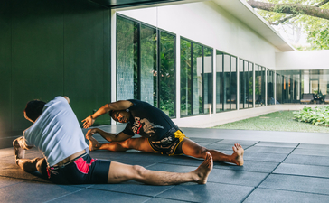 Yoga mat and props arranged on a stone terrace at Amansara, with green walls and glass doors beyond.