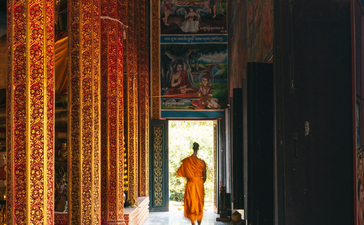 Monk walking through illuminated temple corridor at Amansara, Cambodia.