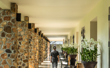 Colonnade with stone pillars at Amansara, dappled light creating shadows along the covered walkway.