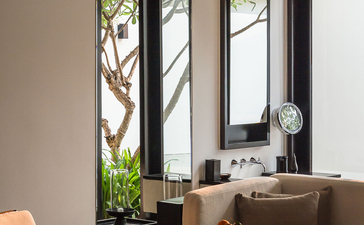 Workspace at Amansara with desk, chair, and tall mirror reflecting garden views through windows.