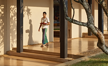 A guest stands in a villa's open-air pavilion at Amanwella, framed by timber columns and overlooking manicured gardens.