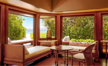 Amanpulo resort Beach Casita interior with daybed, lounge chair and views to tropical gardens through red-framed windows.