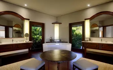 Amanpulo resort spa treatment room with twin vanities, circular soaking tub, and verdant garden views through arched windows.