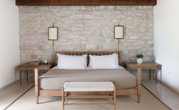 Principal bedroom at Aman Sveti Stefan with wooden bed, neutral stone wall, and soft pendant lighting.