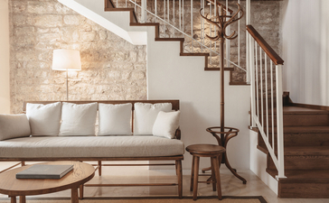Deluxe Cottage living area with neutral sofa, wooden staircase and arched stone details at Aman Sveti Stefan.