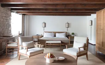 Deluxe cottage bedroom at Aman Sveti Stefan with wooden beams, neutral furnishings, and seated area overlooking Montenegro's coast.