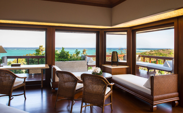 Deluxe Hillside Casita interior at Amanpulo with floor-to-ceiling windows overlooking tropical gardens and ocean views, furnished with wooden desk and seating.