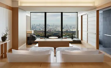 Deluxe Palace Garden View Room at Aman Tokyo with platform bed, floor-to-ceiling windows overlooking the city, and minimalist décor.
