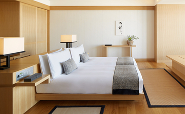 Deluxe Room at Aman Tokyo with pale wood furnishings, white bedding, and floor-to-ceiling windows overlooking the city.