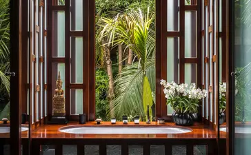 Wooden doors opening onto tropical garden views at Amanpuri resort, Thailand.