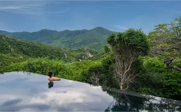 Plunge pool overlooking forested mountains at Amanoi, Vietnam, with a solitary figure seated by the water's edge.
