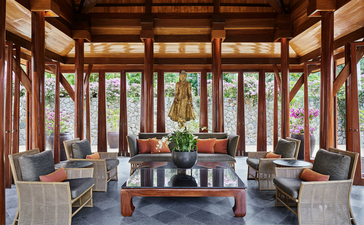 Spacious sitting area in a four-bedroom garden villa at Amanpuri resort, with teak woodwork, floor-to-ceiling windows, and views over the tropical gardens.