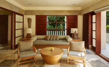 Four-bedroom villa living area at Aman Villas at Nusa Dua, Bali, with wooden furnishings and garden views.