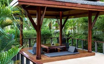 Wooden pavilion with open sides at Amanpuri resort, featuring comfortable seating and views of tropical gardens.