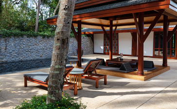 Pabellón junto a la piscina con estructura de madera, asientos y vistas al jardín en Amanpuri.
