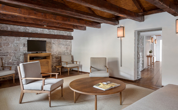 Grand Cottage living room at Aman Sveti Stefan, Montenegro, with wooden beams, stone fireplace and minimal furnishings.