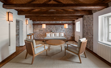 Grand Cottage dining room at Aman Sveti Stefan with wooden ceiling, stone walls, and dining table with chairs.