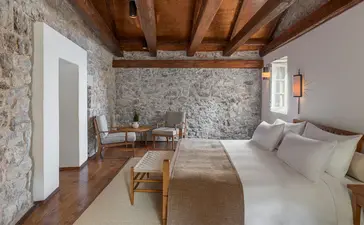 Grand Cottage bedroom at Aman Sveti Stefan with wooden beams, stone walls and twin beds.
