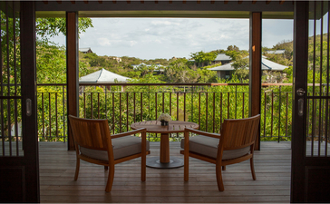 Two chairs and a table on a wooden deck at Amanoi, Vietnam, overlooking verdant hills.
