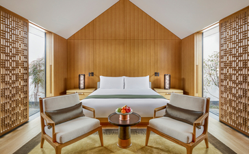 明轩卧室，养云安缦度假村。木制A字形床头墙，两侧对称扶手椅，中央小茶几。