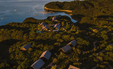 Wooden pathway winds through moss-covered rocks towards the sea at Amanemu resort, Japan.