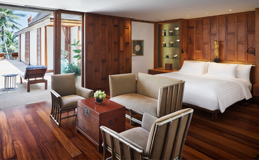 アマンプリのナインベッドルームオーシャンヴィラの広々とした主寝室。木製の床と壁、天蓋ベッド、快適な座席エリアを備えている。